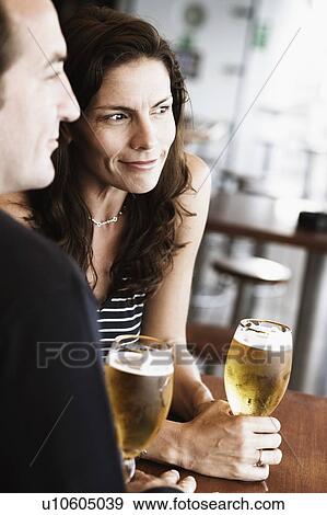Mid adult couple sitting in a bar and holding beer in stem glasses View Large Photo Image Stock Photo - Mid adult couple sitting in a bar and holding beer in stem glasses. Fotosearch