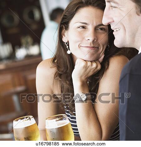 Stock Photography - Mid adult couple sitting in a bar and holding beer in stem glasses. Fotosearch