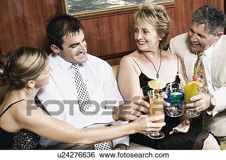Stock Photograph - Mid adult couple with a mature woman and a senior man toasting glasses of cocktail. Fotosearch