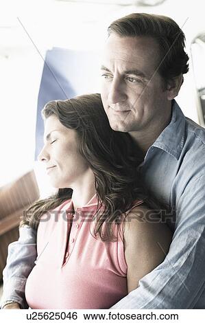Stock Photograph - Mid adult man embracing a mid adult woman from behind. Fotosearch