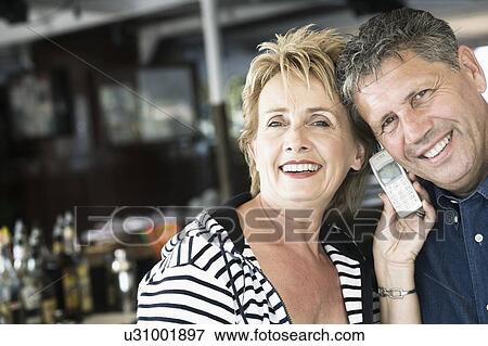 Portrait of a mature woman and a senior man listening to a mobile phone and smiling View Large Photo Image Stock Photo - Portrait of a mature woman and a senior man listening to a mobile phone and smiling. Fotosearch
