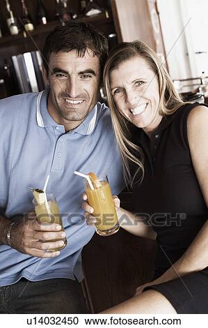 Stock Image - Portrait of a mid adult couple holding glasses of juice and smiling. Fotosearch