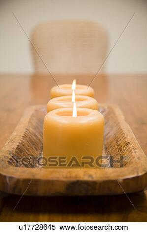 Stock Photography - Detail of three lit candles on wooden holder. Fotosearch