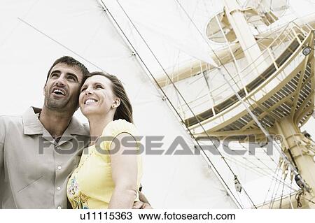 Stock Image - Low angle view of a mid adult couple on a sailing ship and smiling. Fotosearch