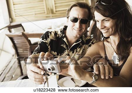 Mid adult couple looking at a digital camera in a restaurant View Large Photo Image Stock Photo - Mid adult couple looking at a digital camera in a restaurant. Fotosearch
