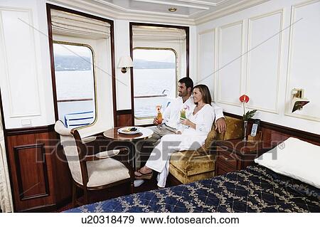 Mid adult couple sitting in a cabin of a sailing ship and holding glasses of cocktail and smiling View Large Photo Image Stock Photo - Mid adult couple sitting in a cabin of a sailing ship and holding glasses of cocktail and smiling. Fotosearch