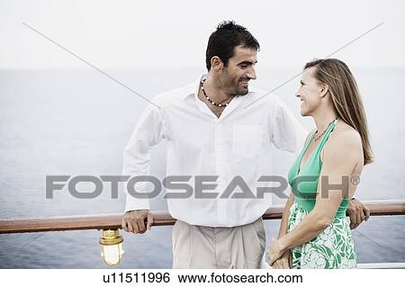 Stock Photograph - Mid adult couple standing near a railing and looking at each other. Fotosearch
