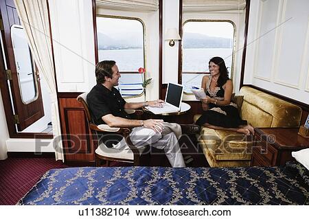 Picture - Mid adult man using a laptop with a mid adult woman holding a book and smiling. Fotosearch