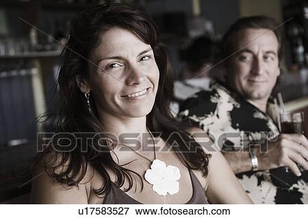 Stock Photo - Mid adult woman smiling with a mid adult man holding a glass of drink beside her. Fotosearch