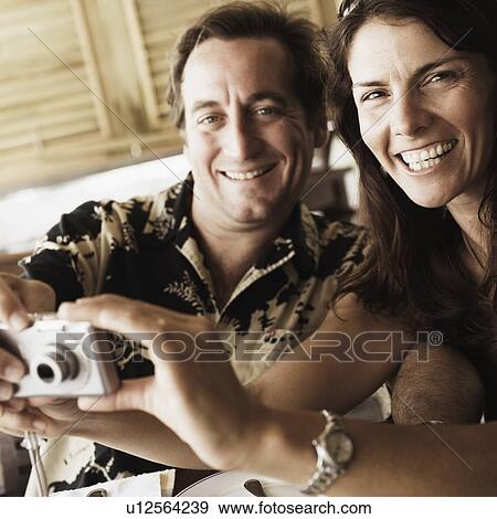 Portrait of a mid adult couple holding a digital camera in a restaurant View Large Photo Image Stock Photo - Portrait of a mid adult couple holding a digital camera in a restaurant. Fotosearch