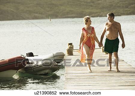 Senior man and a mature woman holding each other's hands and walking on a jetty View Large Photo Image Stock Image - Senior man and a mature woman holding each other's hands and walking on a jetty. Fotosearch