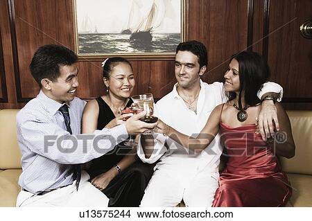 Picture - Two young couples sitting on a couch and toasting their glasses. Fotosearch