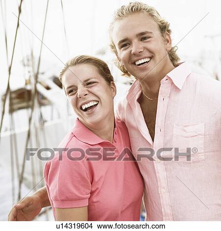 Young couple standing with their arms around each other and smiling View Large Photo Image Picture - Young couple standing with their arms around each other and smiling. Fotosearch