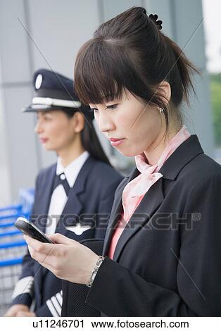Close-up of a female cabin crew holding a mobile phone with a female pilot standing in the background View Large Photo Image Stock Image - Close-up of a female cabin crew holding a mobile phone with a female pilot standing in the background. Fotosearch