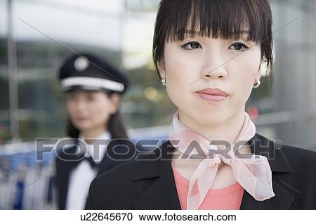 Stock Image - Close-up of a female cabin crew looking away with a female pilot behind her. Fotosearch