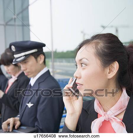Stock Photo - Close-up of a female cabin crew talking on a mobile phone with a pilot using a laptop in the background. Fotosearch