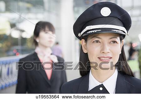 Picture - Close-up of a female pilot smiling with a female cabin crew behind her. Fotosearch