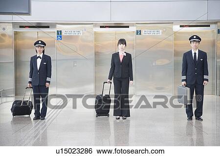 Stock Photograph - Male and a female pilot standing with a female cabin crew in front of elevators. Fotosearch