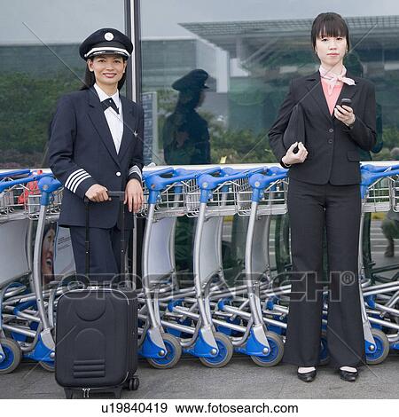 Portrait of a female cabin crew holding a mobile phone and standing with a female pilot at an airport View Large Photo Image Stock Photo - Portrait of a female cabin crew holding a mobile phone and standing with a female pilot at an airport. Fotosearch
