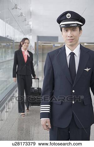 Stock Photo - Portrait of a male pilot with a female cabin crew walking behind him. Fotosearch