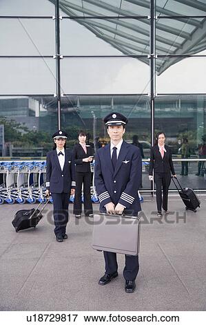 Portrait of a pilot holding a briefcase with a female pilot and two cabin crews standing in the background View Large Photo Image Stock Photo - Portrait of a pilot holding a briefcase with a female pilot and two cabin crews standing in the background. Fotosearch