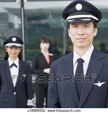 Stock Image - Portrait of a pilot with a female pilot and a cabin crew standing in the background. Fotosearch