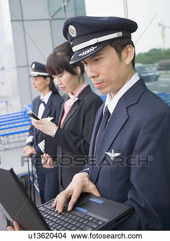 Side profile of a female cabin crew holding a mobile phone and standing with two pilots at an airport View Large Photo Image Picture - Side profile of a female cabin crew holding a mobile phone and standing with two pilots at an airport. Fotosearch
