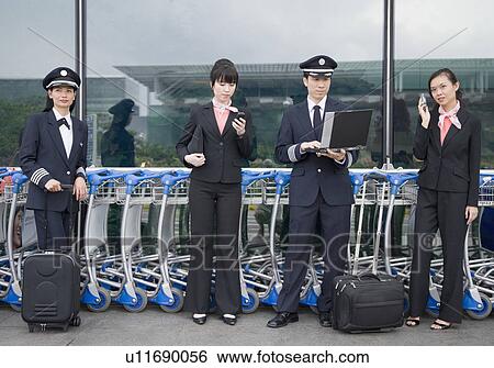 Two female cabin crews holding mobile phones and standing with two pilots at an airport View Large Photo Image Stock Photograph - Two female cabin crews holding mobile phones and standing with two pilots at an airport. Fotosearch