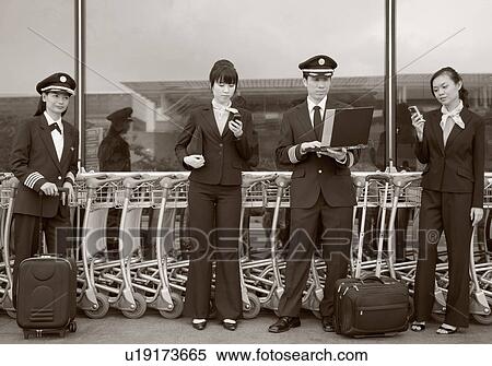 Two female cabin crews holding mobile phones and standing with two pilots at an airport View Large Photo Image Stock Photography - Two female cabin crews holding mobile phones and standing with two pilots at an airport. Fotosearch