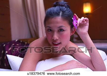 Stock Photograph - Young womain holding a flower, looking at camera, close-up. Fotosearch