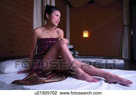 Stock Image - Young womain sitting in spa room, smiling, full length. Fotosearch