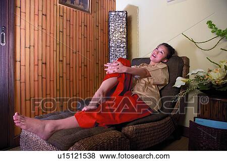 Young woman sitting on sofa, holding knee View Large Photo Image Stock Photo - Young woman sitting on sofa, holding knee. Fotosearch