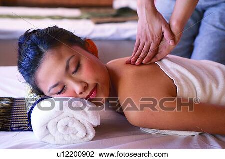 Stock Image - Young woman wearing towel, getting a massage with eyes closed, side view. Fotosearch