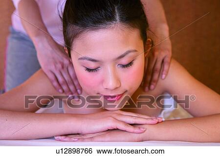 Stock Photograph - Young woman wearing towel, getting a massage with eyes closed, front view. Fotosearch