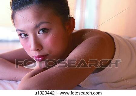 Stock Image - Young woman wearing towel, lying on front, looking at camera, close-up. Fotosearch