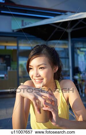 Stock Photo - Young Lady Sitting at Outdoor Cafe, Holding Cold Drink, Looking Away. Fotosearch