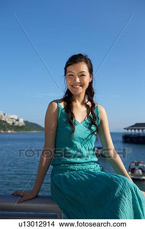 Picture - Young Lady Sitting on Railing of Fence, Smiling. Fotosearch