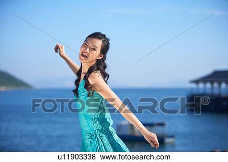 Stock Photo - Young Lady Standing with Arms Outstretched, Smiling. Fotosearch