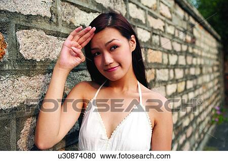 Stock Image - Young woman leaning on wall, smiling. Fotosearch