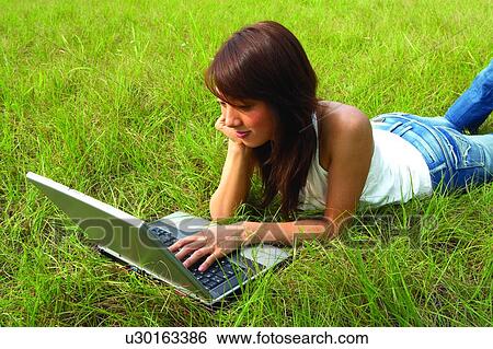 Young woman lying on grass, using notebook computer View Large Photo Image Stock Photograph - Young woman lying on grass, using notebook computer. Fotosearch
