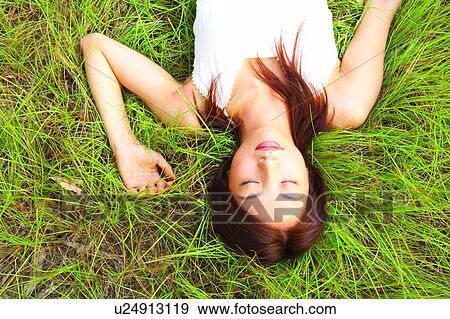 Stock Photo - Young woman lying on grass with eyes closed. Fotosearch