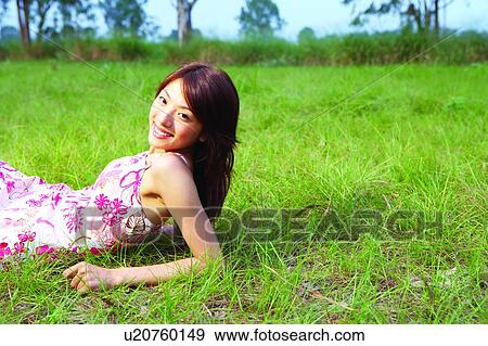 Stock Photo - Young woman lying on grass with upper body up, looking at camera. Fotosearch