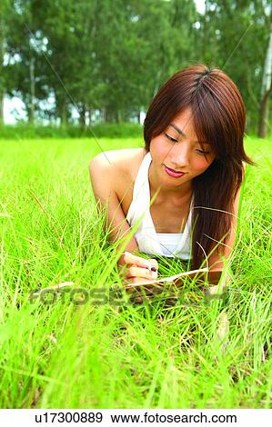 Stock Photo - Young woman lying on grass writing. Fotosearch