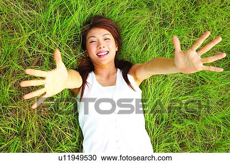 Stock Image - Young woman lying on long grass, hands open. Fotosearch