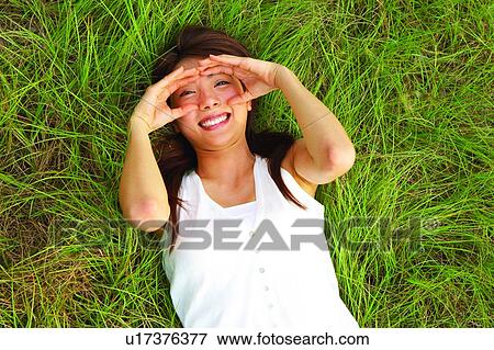 Stock Photo - Young woman lying on long grass, hands cupped with toothy smile. Fotosearch