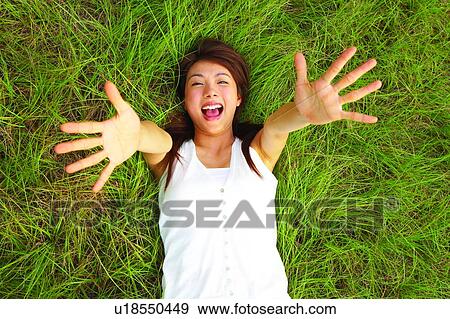 Stock Photo - Young woman lying on long grass, hands open, close-up. Fotosearch