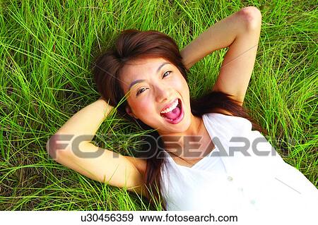 Stock Photo - Young woman lying on long grass hands behind head. Fotosearch