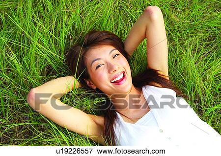 Young woman lying on long grass, smiling cheerfully, hands behind head, close-up View Large Photo Image Stock Photo - Young woman lying on long grass, smiling cheerfully, hands behind head, close-up. Fotosearch