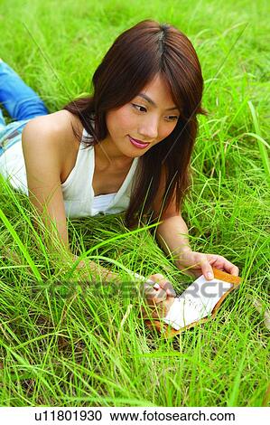 Young woman lying on long green grass, writing View Large Photo Image Stock Image - Young woman lying on long green grass, writing. Fotosearch
