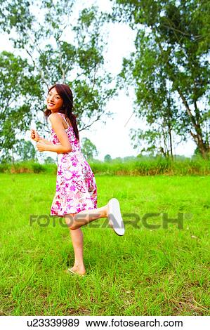 Stock Photo - Young woman running on grasslands, laughing. Fotosearch
